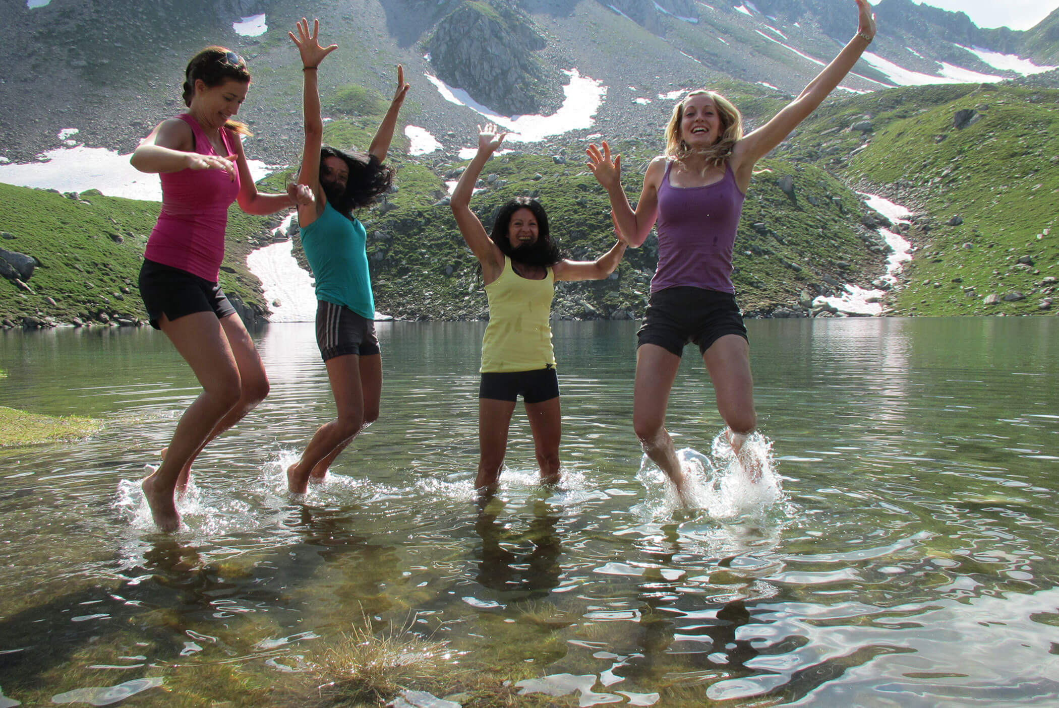 Four women jump and splash in a mountain lake, smiling and raising their arms on a sunny day. - Residence Aichner