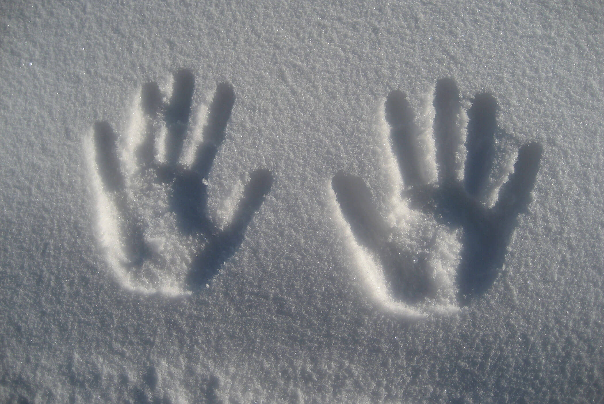 Zwei Handabdrücke, die in den frischen, weißen Schnee gedrückt wurden und deutliche Abdrücke der Finger und der Handfläche zeigen. - Residence Aichner