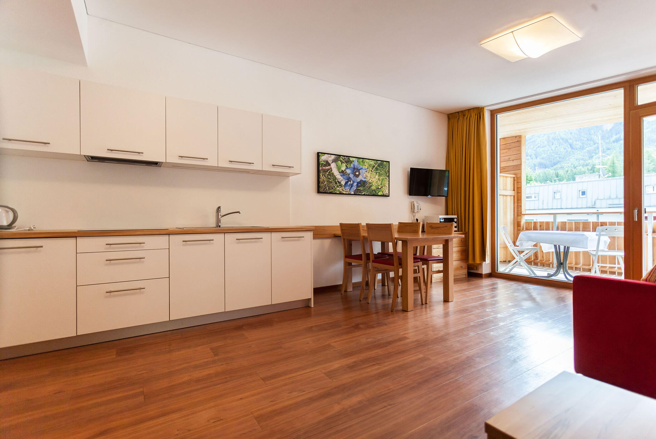 Cucina moderna e zona pranzo con pavimenti in legno, mobili bianchi, portefinestre e vista sulle montagne. - Residence Aichner