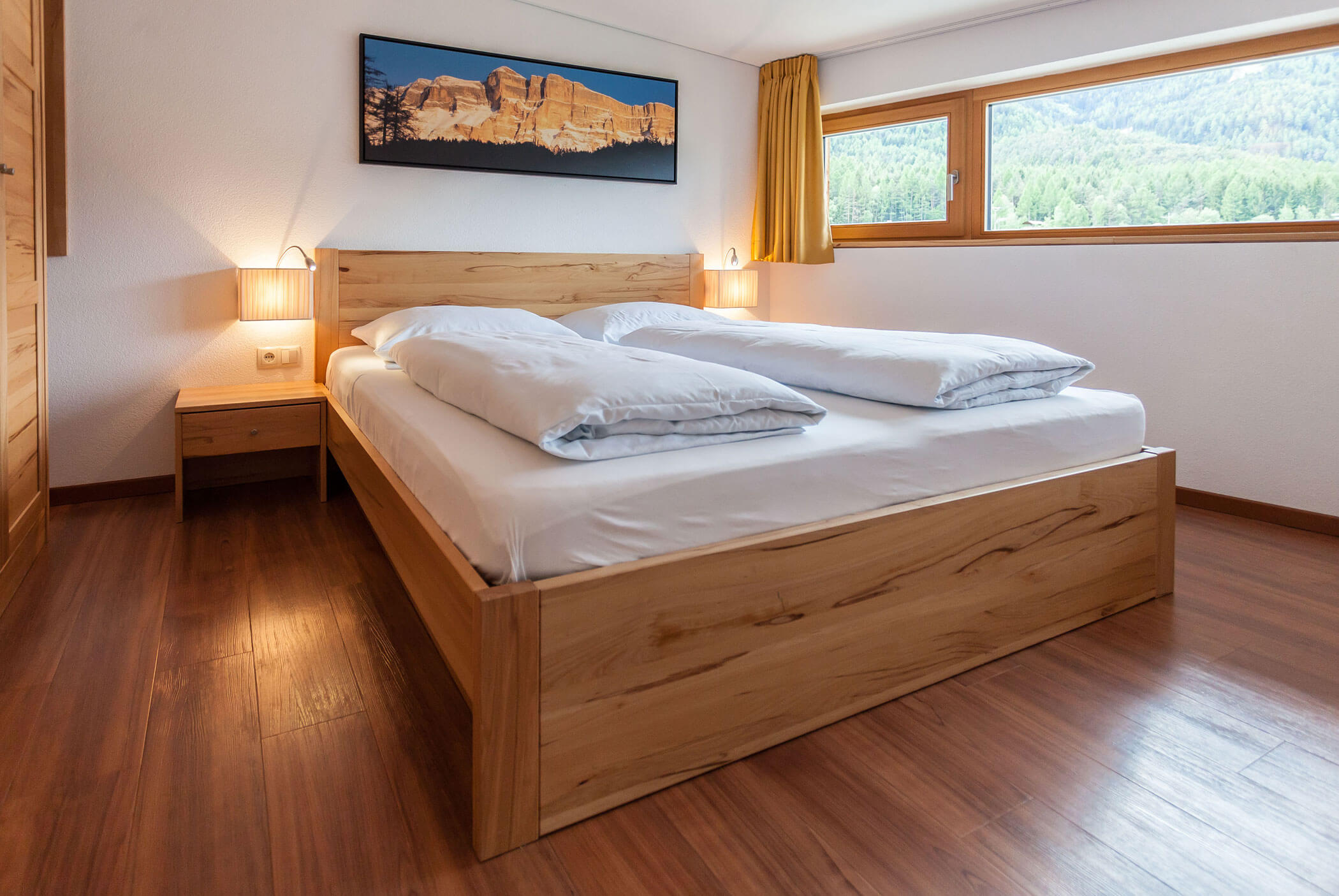 Camera da letto in stile minimalista con letto e pavimento in legno, ampia finestra e una foto di montagna appesa alla parete. - Residence Aichner