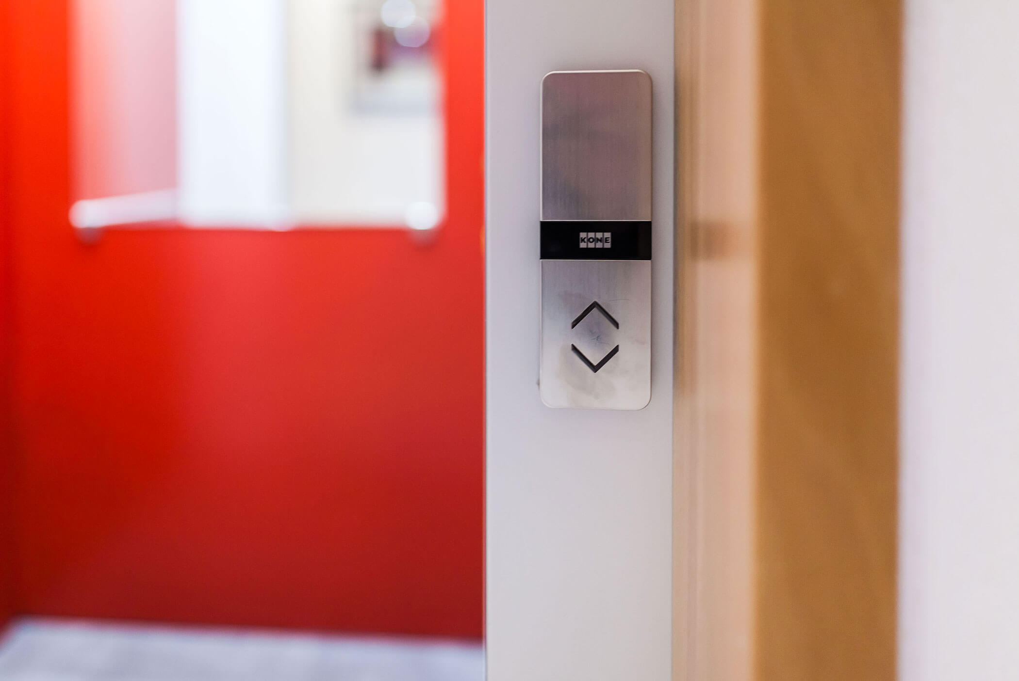Nahaufnahme eines Aufzugsknopffelds mit Auf- und Ab-Pfeilen vor einer roten Wand in einem Flur. - Residence Aichner