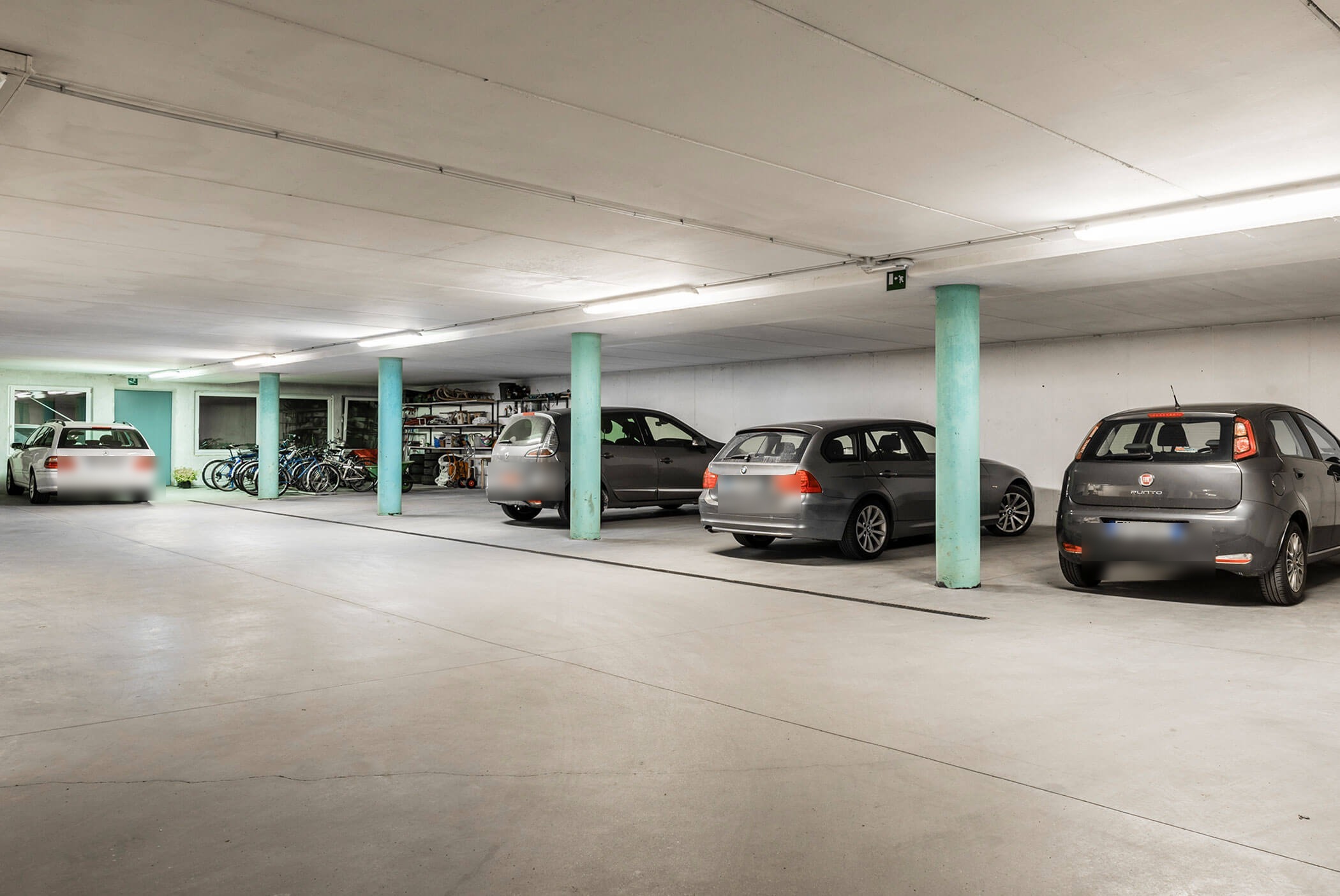Tiefgarage mit vier geparkten Autos, Fahrrädern, Regalen und grünen Säulen. - Residence Aichner