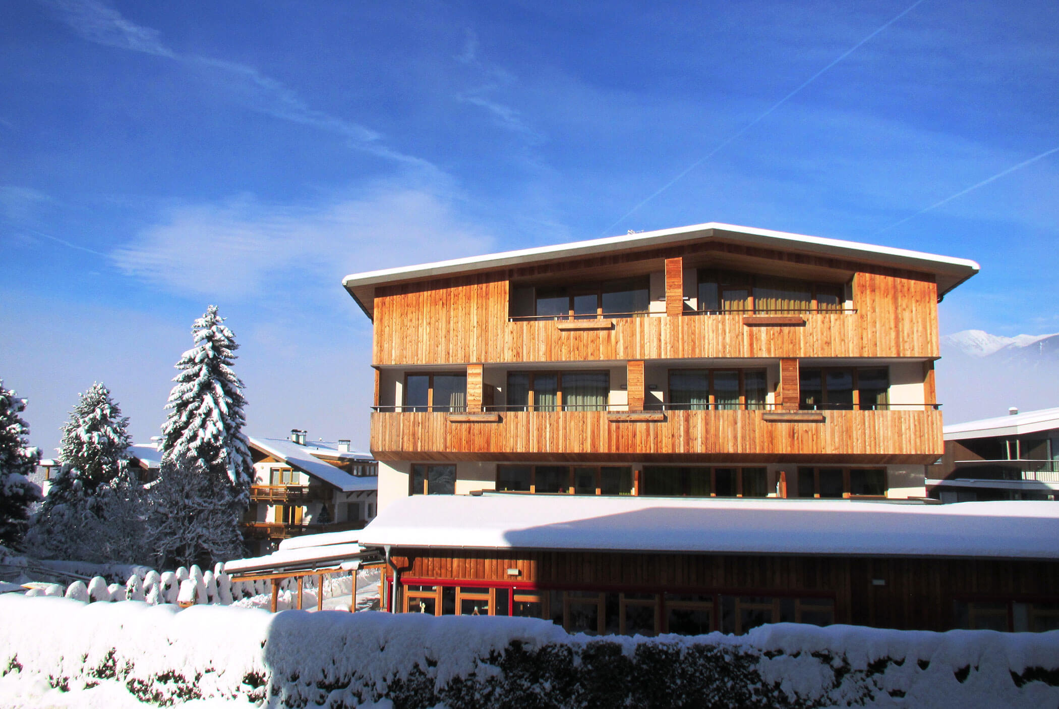 Ein modernes Holzchalet mit Balkonen, umgeben von Schnee und Kiefern unter einem strahlend blauen Himmel. - Residence Aichner