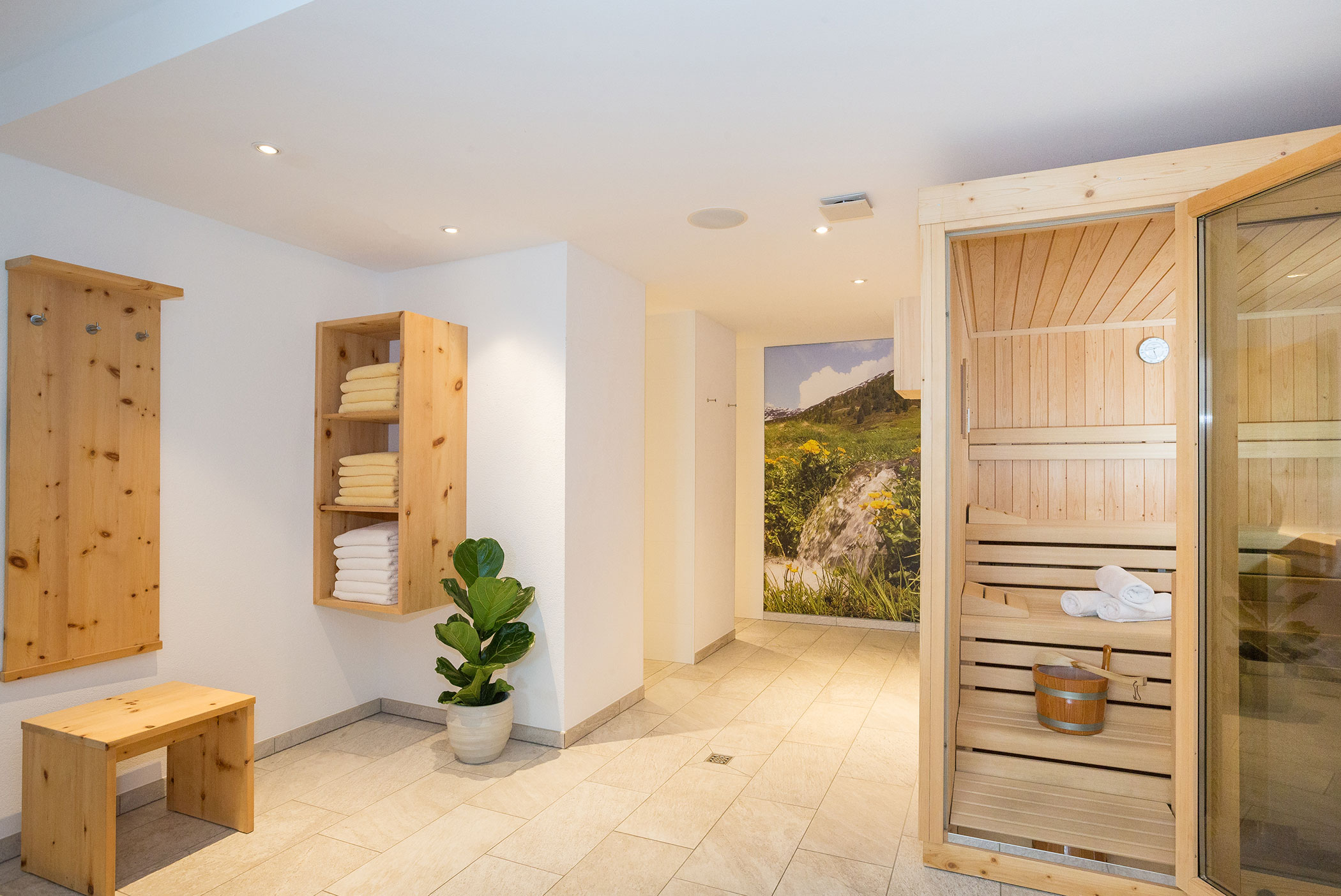 A modern spa room with a wooden sauna, shelves with towels, a bench, and a potted plant. - Residence Aichner