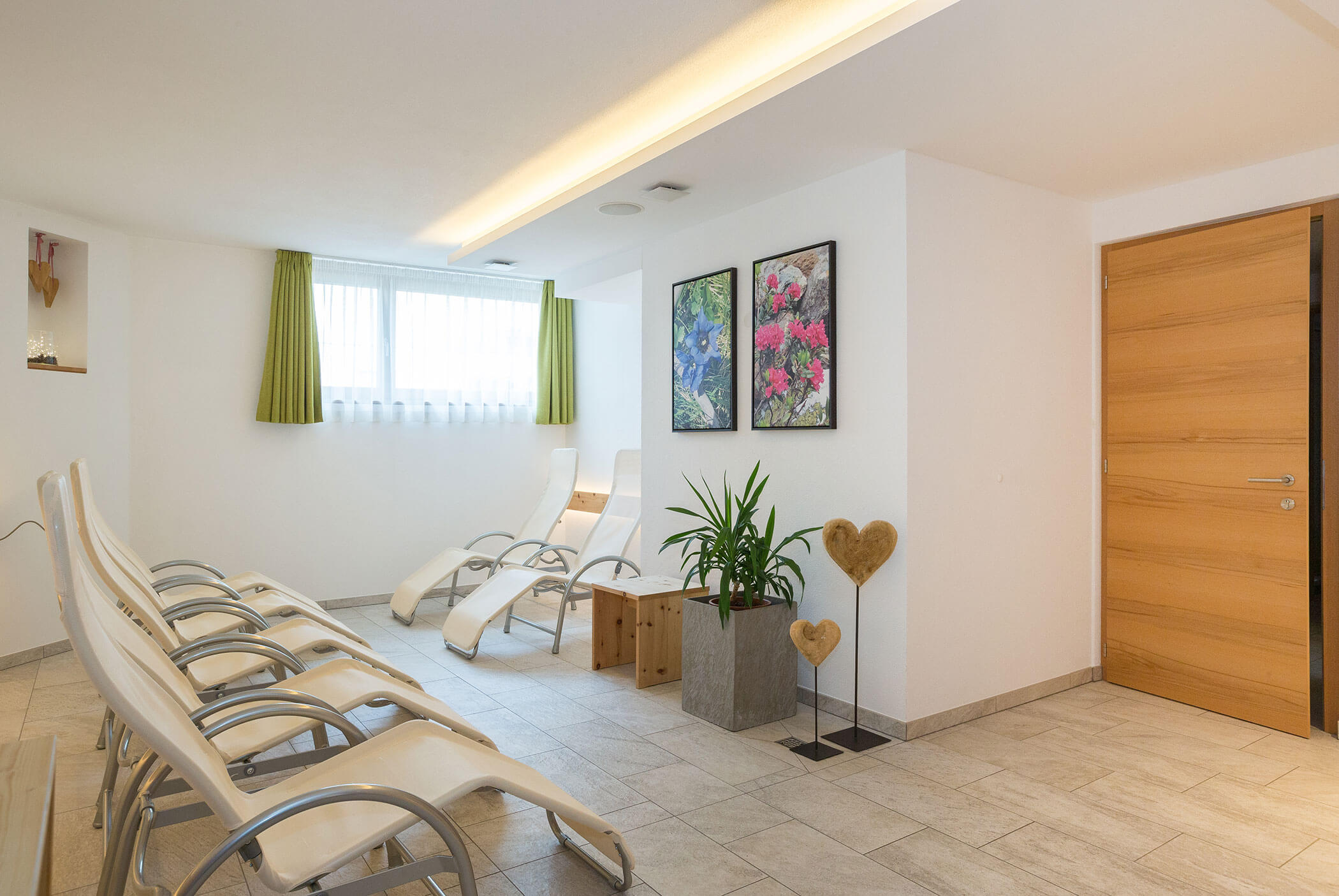 A bright relaxation room with lounge chairs, potted plants, and colorful floral artwork on the wall. - Residence Aichner