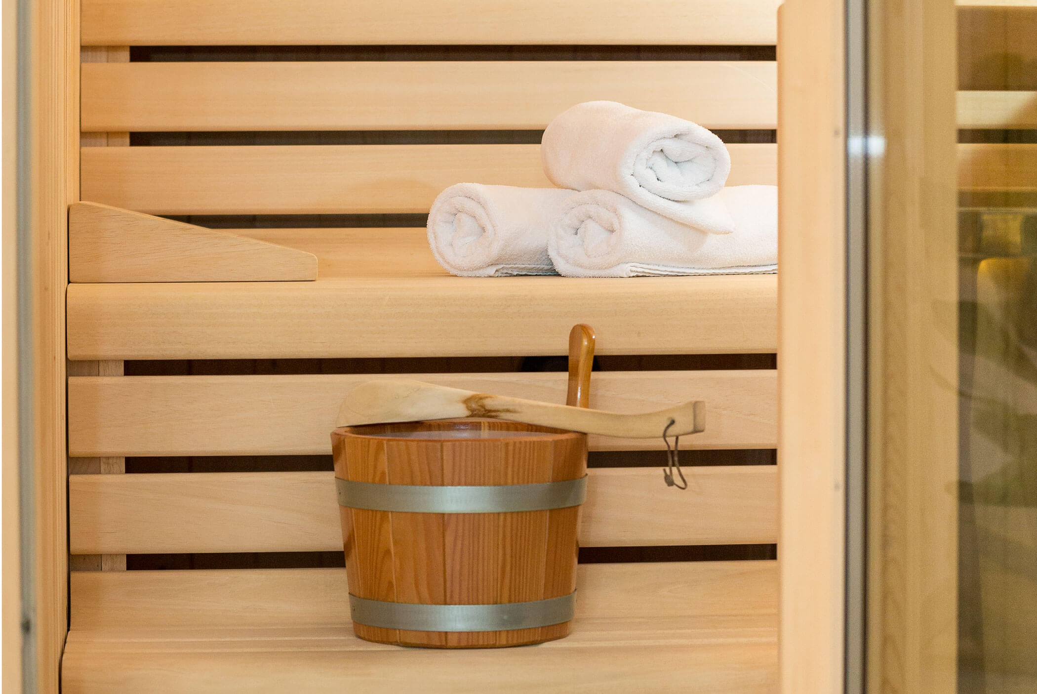 Wooden sauna with a bucket, ladle, and three rolled white towels on the upper bench. - Residence Aichner