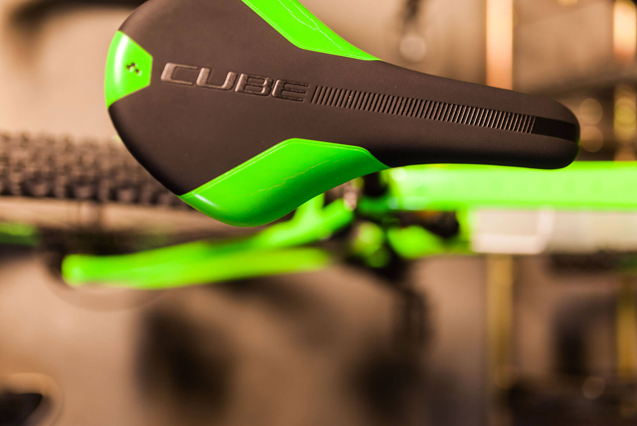 Close-up of a black and green bicycle seat labeled CUBE, with part of the bike frame visible below. - Residence Aichner
