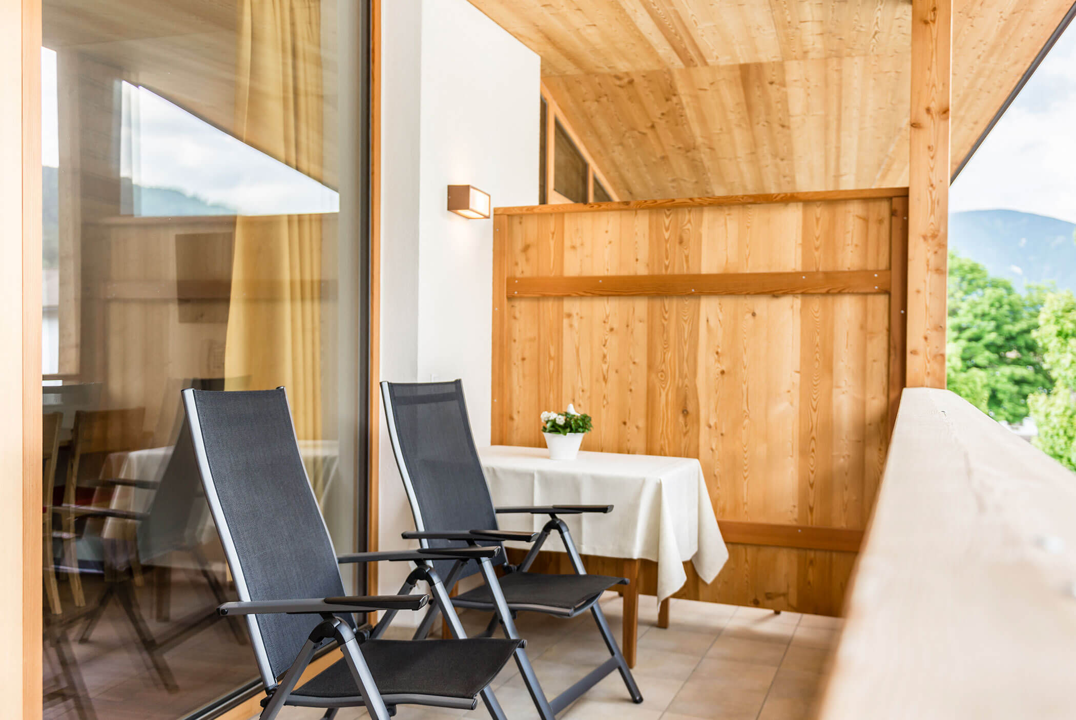 Due sedie nere e un tavolo con una pianta in vaso su un balcone in legno con vista sulle montagne. - Residence Aichner