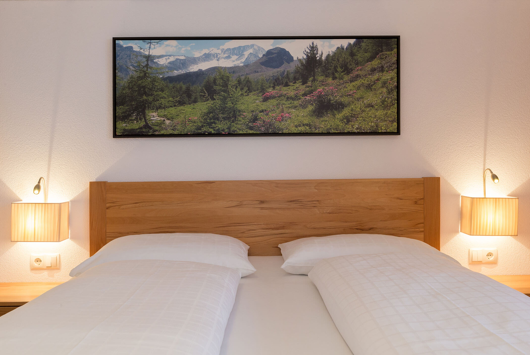 Un letto matrimoniale ben rifatto, con lenzuola bianche, testiera in legno e una foto di un paesaggio appesa sopra. - Residence Aichner