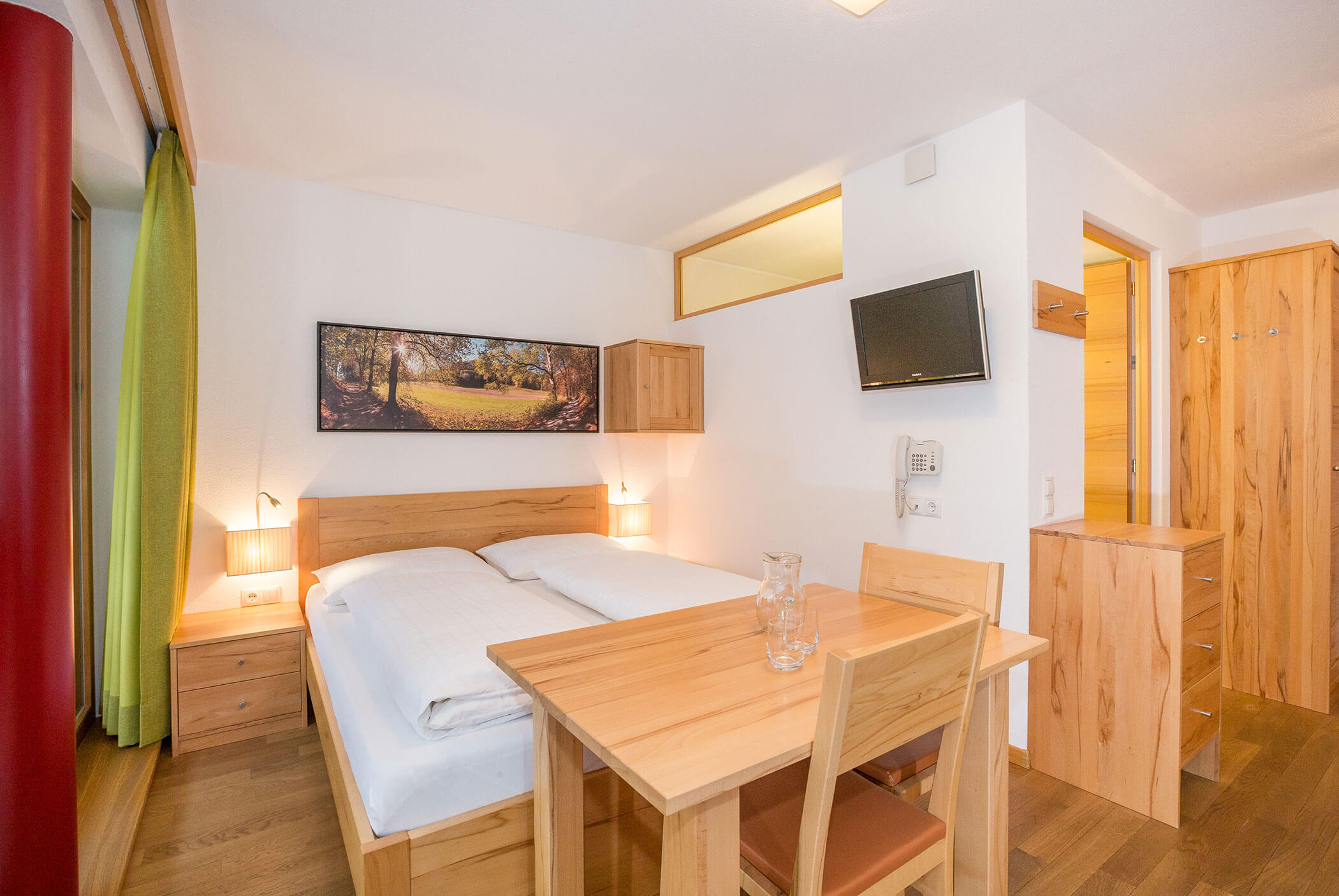 Camera d’albergo luminosa e moderna, dotata di letto, tavolino da pranzo, TV a parete e mobili in legno. - Residence Aichner